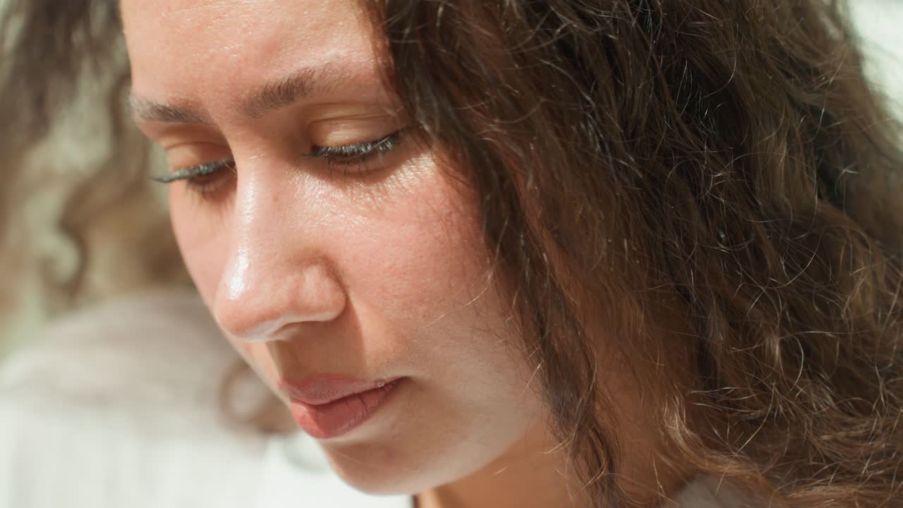Closeup woman face with sand, contemplative traveler writing in notebook in island bungalow, soft sunlit highlights on curly hair, intimate reflective mood, textured skin, subtle freckles, close