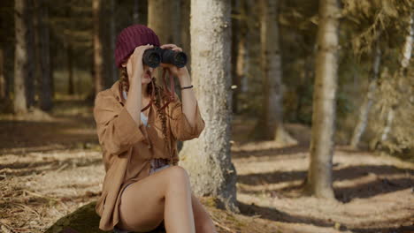 Female-tourist-searching-through-binoculars-in-forest