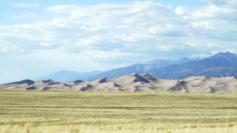 stunning late summer early fall view of the great sand dunes national park colorado rockies mountain sandy 14er peaks crisp golden yellow tall grass wind clouds blue sky mid day cinematic car motion