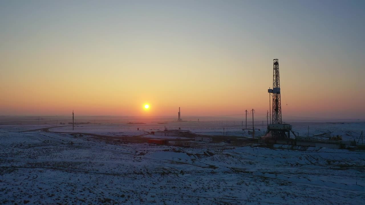 Olieboreplatform ved solnedgang over et sneklædt gasfeltlandskab.