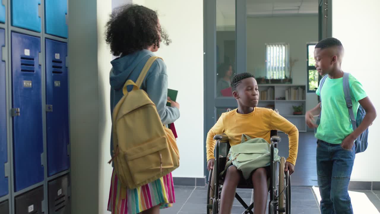 Studenti adolescenti afroamericani che si muovono nel corridoio della scuola, un coetaneo spinge una sedia a rotelle, una ragazza chiacchiera.