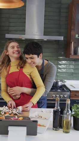 happy caucasian lesbian preparing food,embracing and using tablet in sunny kitchen
