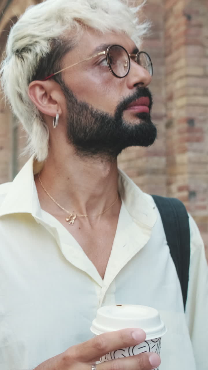 Giovane uomo con capelli decolorati e occhiali che tiene una tazza di caffè all'aperto