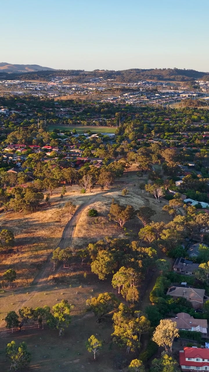 Ripresa con drone che cattura un quartiere residenziale e un'area verde durante l'ora d'oro a Canberra, Australia