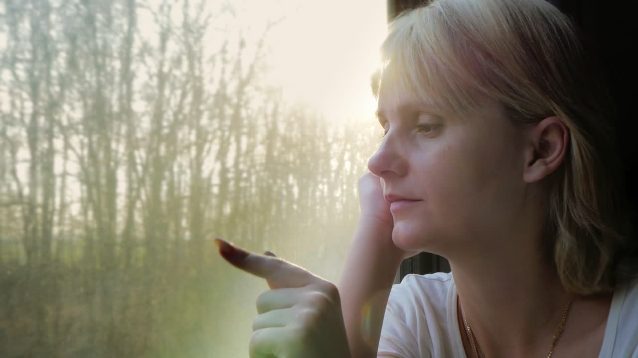 портрет молодой женщины, едущей в поезде, которая смотрит в окно, солнечные лучи освещают ее