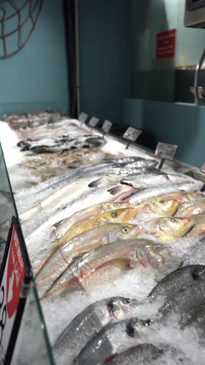 Abundant variety of fresh raw fish and seafood including prawns, shrimps, and mussels displayed on a bed of crushed ice at a grocery store counter for customers to choose from