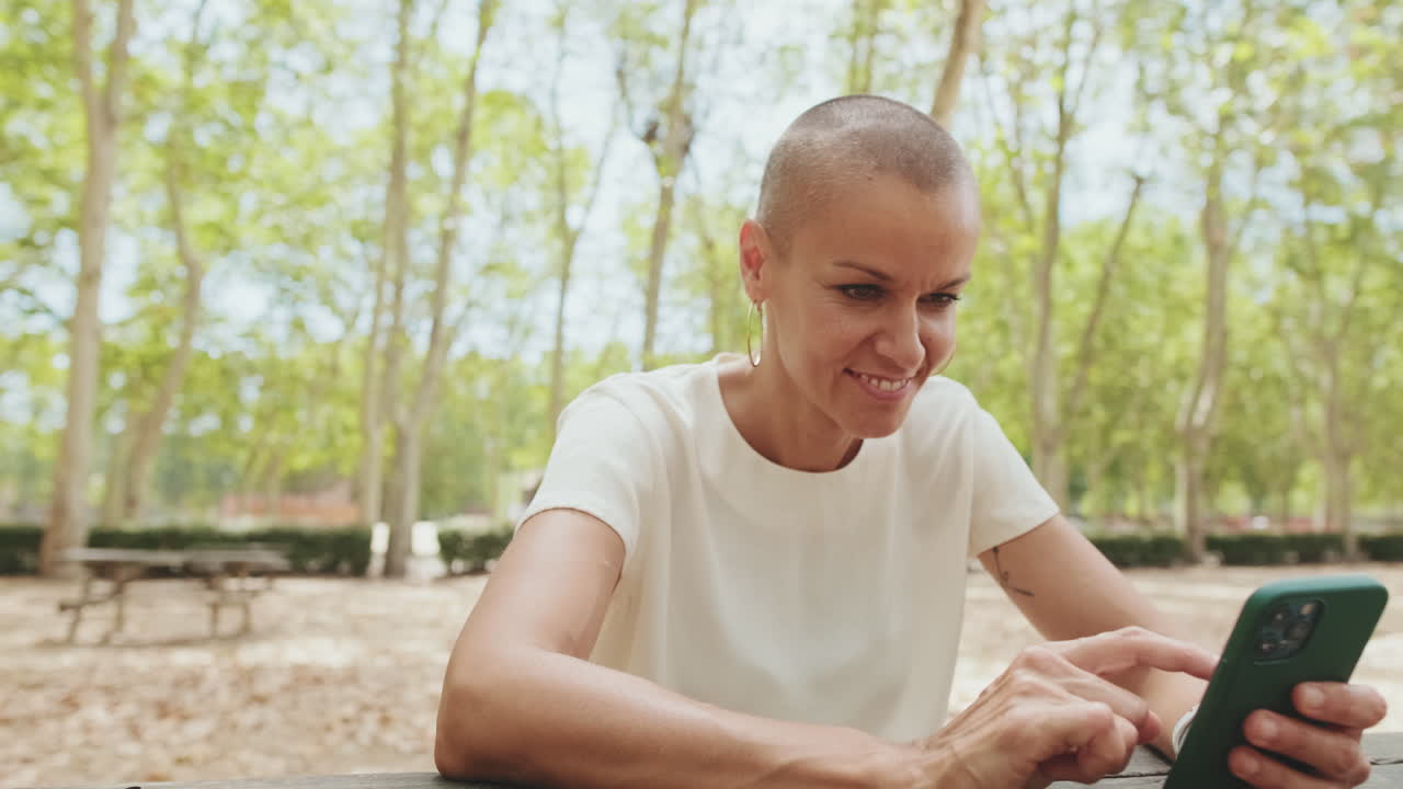 Donna calva sorridente che usa lo smartphone all'aperto in un parco