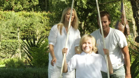 happy parents help their son on a swing