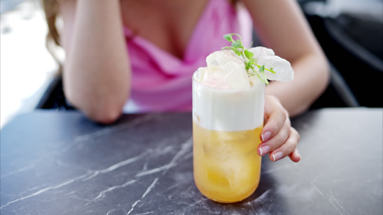 Woman holding a summer white and orange cocktail with whiskey and peach juice, slow motion