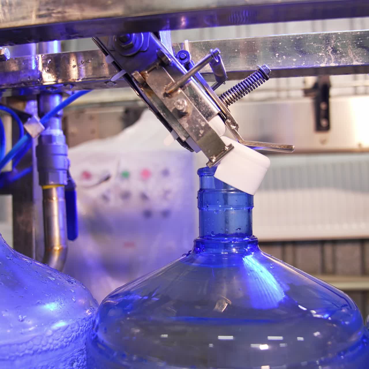 Conveyor belt with big blue flasks moving slowly. Bottles are filled with clean mineral water and being corked