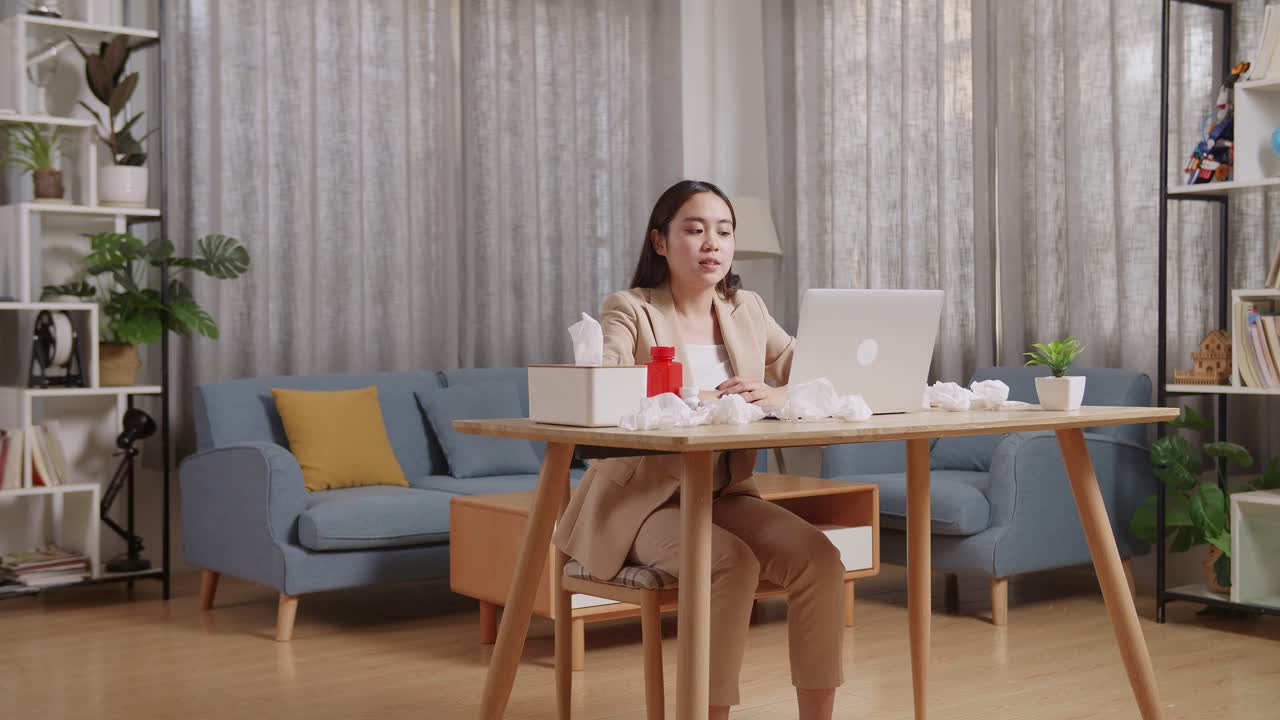 아픈 아시아 사업가 여성이 집에서 일하는 동안 노트북에서 의사와 비디오 통화를 하는 데 온도계를 들고 있습니다.