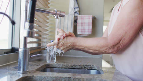 mid section of senior caucasian woman washing her hands in the sink at home