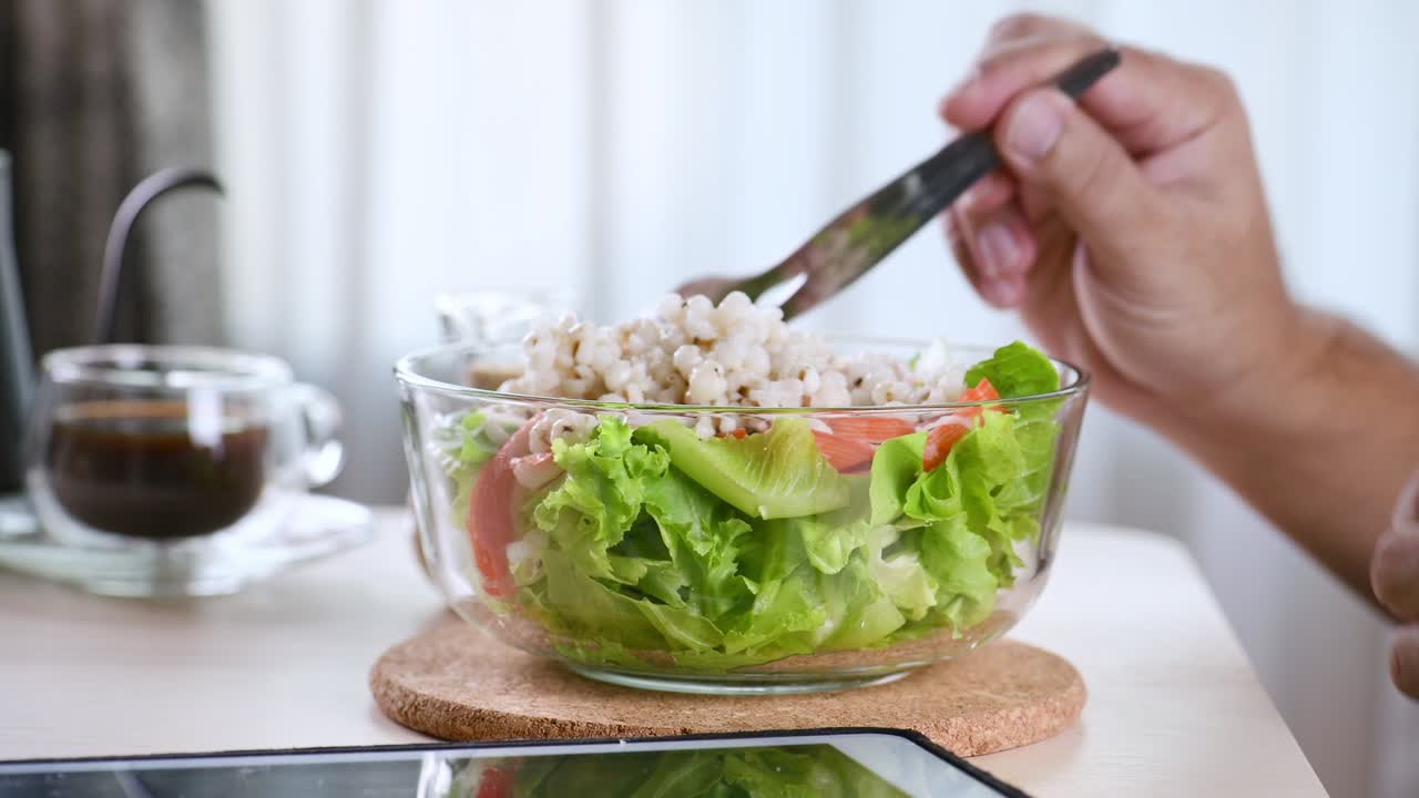 아내는 아침 식사 테이블에서 남편에게 초록색 채소 러드 한 그을 제공합니다. 신선한 러드를 먹고 깨한 채소가 생으로 먹을 수 있습니다. 음식을 먹고, 커피를 마시고, 터치 스크린 태블릿 컴퓨터 태블릿을 보고 슬라이드를 표시합니다.