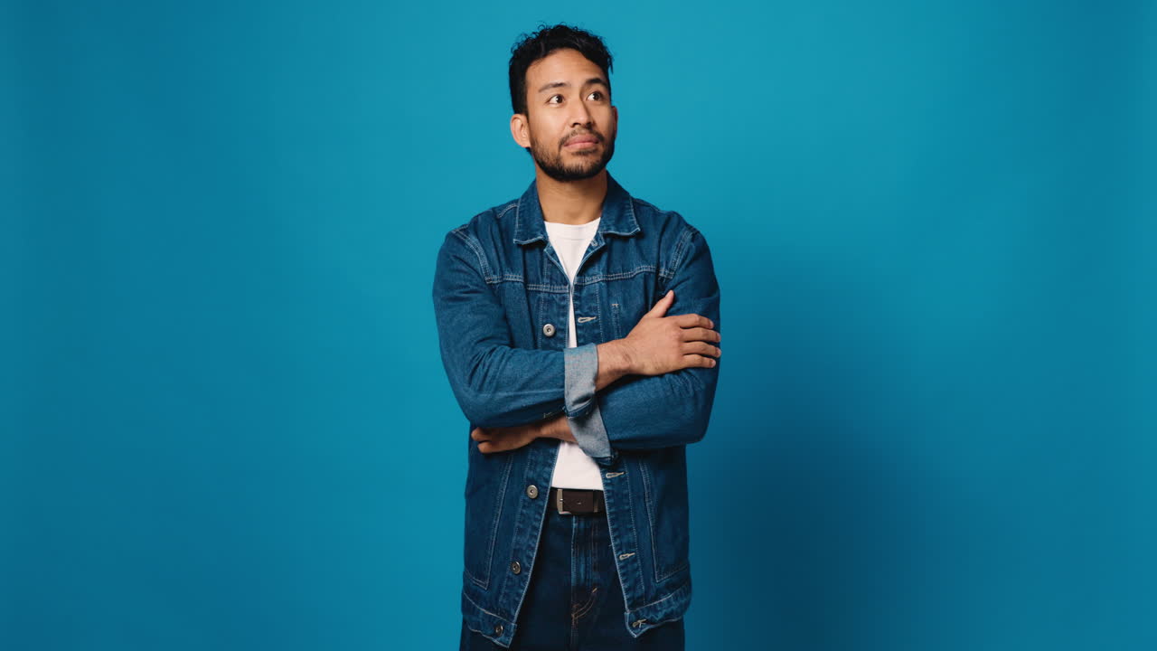 A man in a denim jacket smiles against a blue backdrop