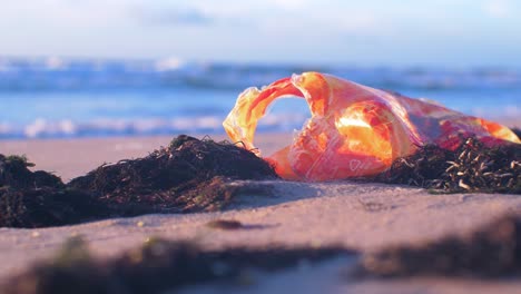 Plastic-packaging-on-the-beach,-trash-and-waste-litter-on-an-empty-Baltic-sea-white-sand-beach,-environmental-pollution-problem,-golden-hour-light-on-evening,-closeup-shot