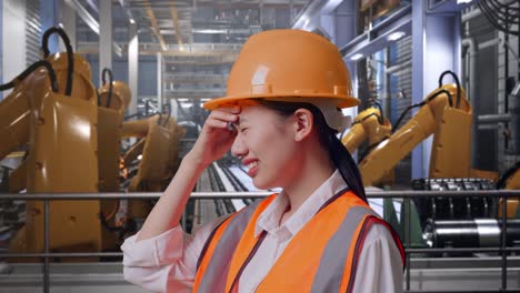 close up side view of asian female engineer with safety helmet having a headache while working with industrial robotic arms working