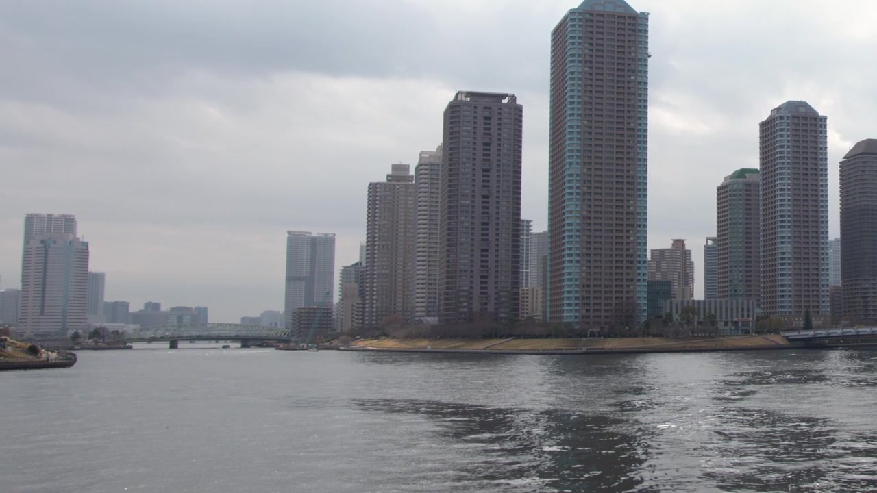 Wide shot of Tokyo skyscrapers along the Sumida River under overcast skies in Japan.