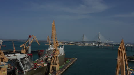 Aerial---Container-ship-and-cranes-at-dock-in-Cadiz,-Spain,-wide-shot-approach