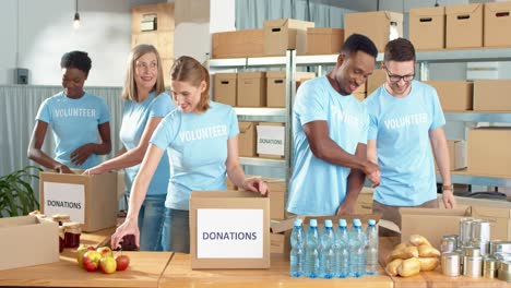 multiethnic group of volunteers working and packing boxes with food and clothes in charity warehouse