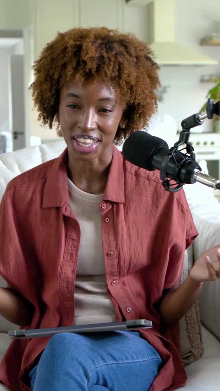 Video verticale: Avvio podcast, donna conduttrice in camicia color ruggine che parla al microfono sul divano, usando un tablet.