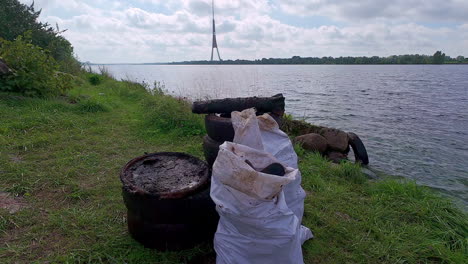 discarded rubber tyres and white trash sack on a riverbank overlooking the daugava river in riga, latvia