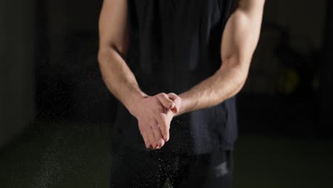 Unrecognizable-male-athlete-rubbing-and-clapping-chalk-at-gym