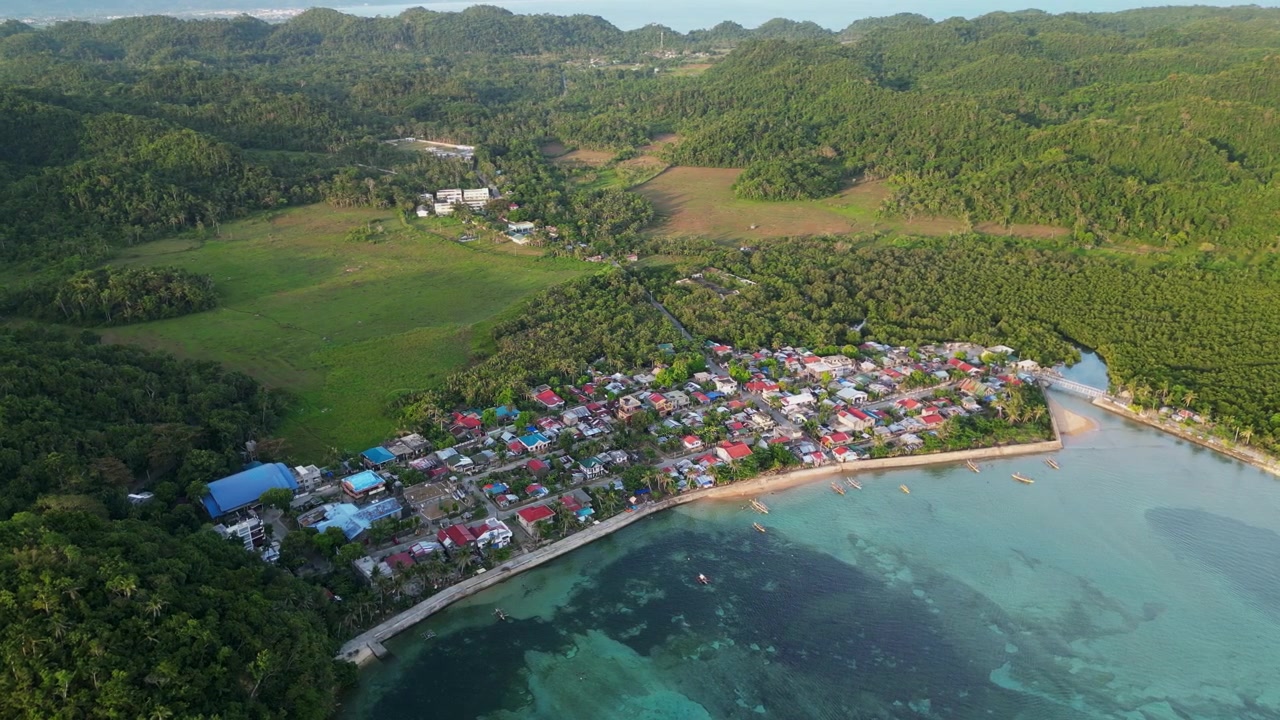 Vista aerea panoramica orbitante di un villaggio di pescatori costiero barangay tra la lussureggiante vegetazione tropicale dell'isola - Magnesia Del Norte, Catanduanes, Filippine