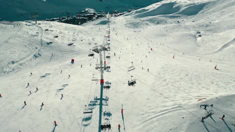 Busy-ski-resort-ski-slopes,-skiers-and-snowboarders-down-mountainside,-aerial