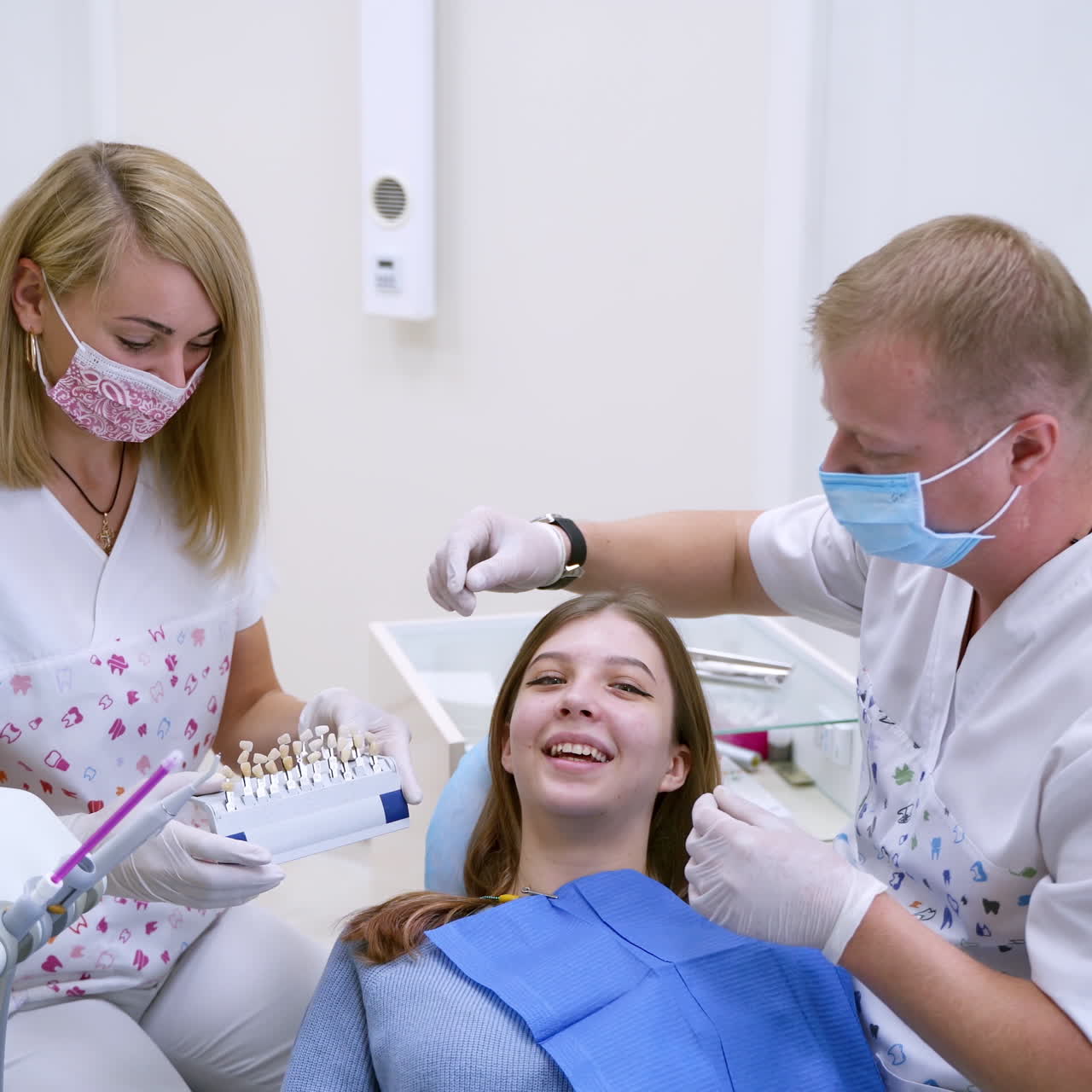 Dentist with assistant work with patient.Professional stomatologist chooses the color of artificial tooth for smiling woman. Benefits of tooth implants.