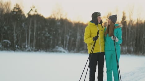 a man in a yellow jacket and a girl in a blue jumpsuit skiing in slow motion at sunset