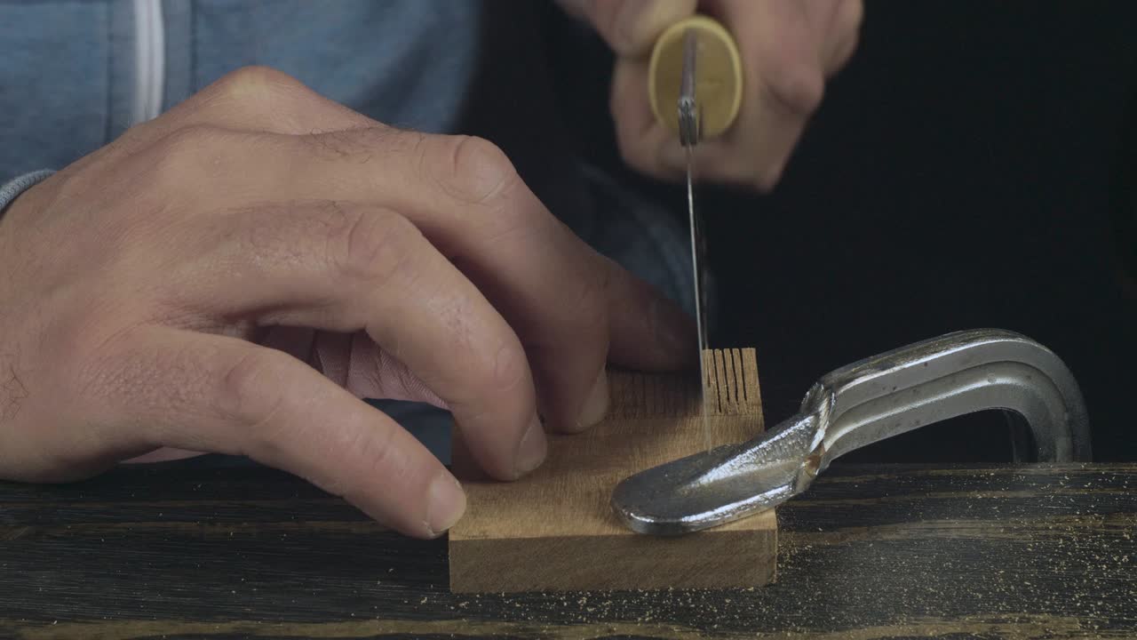 primer plano de las manos del hombre aserrando un detalle de madera con una sierra de mano. carpintero hace un peine de madera hecho a mano. cine 4k video