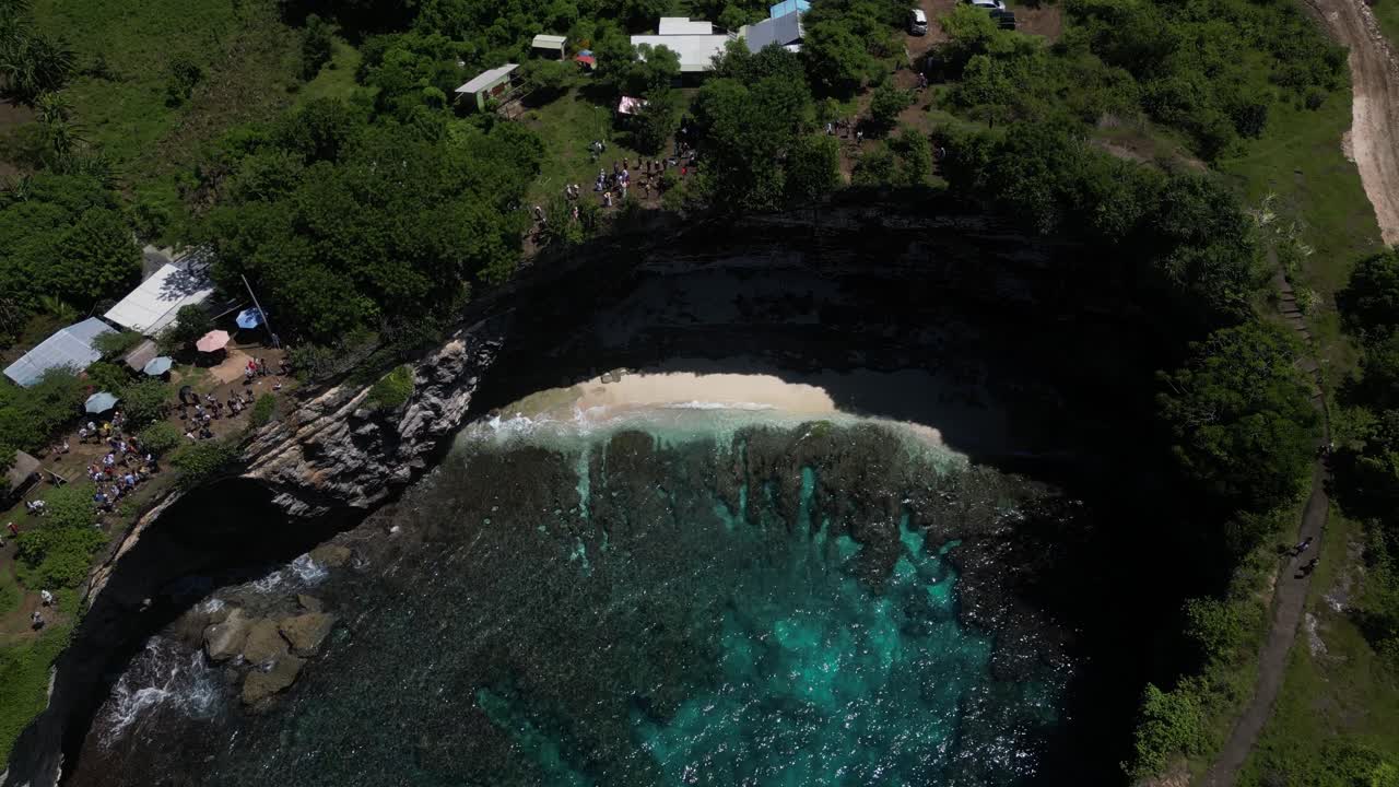 un agujero de agua rodeado de acantilados con agua clara y una pequeña playa en la isla de nusa penida, indonesia