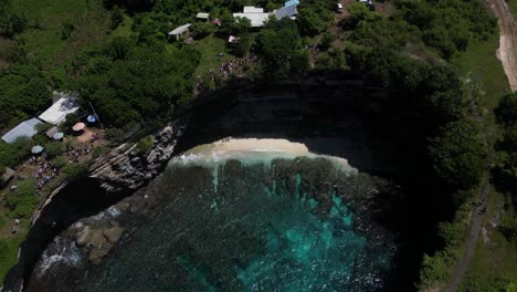 A-hole-of-water-surrounded-by-cliffs-with-clear-water-and-a-small-beach-on-the-island-of-Nusa-Penida,-Indonesia