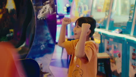 young asiatic girl celebrate a victory at the amusement park, slow motion kid raising her arms while playing games