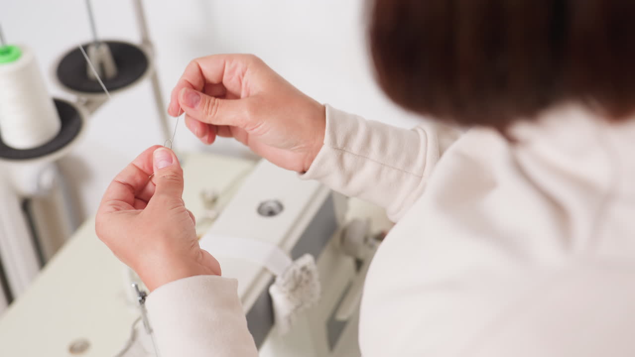Side view of costumer skillfully tying thread knot on sewing machine, highlighting manual precision, dexterity, apparel creation, confident technique, and steady approach in well lit workspace