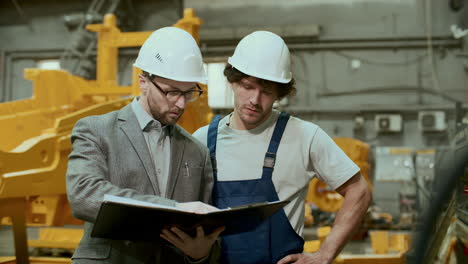 engineer discussing technical drawings with mechanic in industrial factory