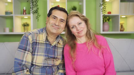 happy and sympathetic husband and wife are looking at camera and smiling at home.