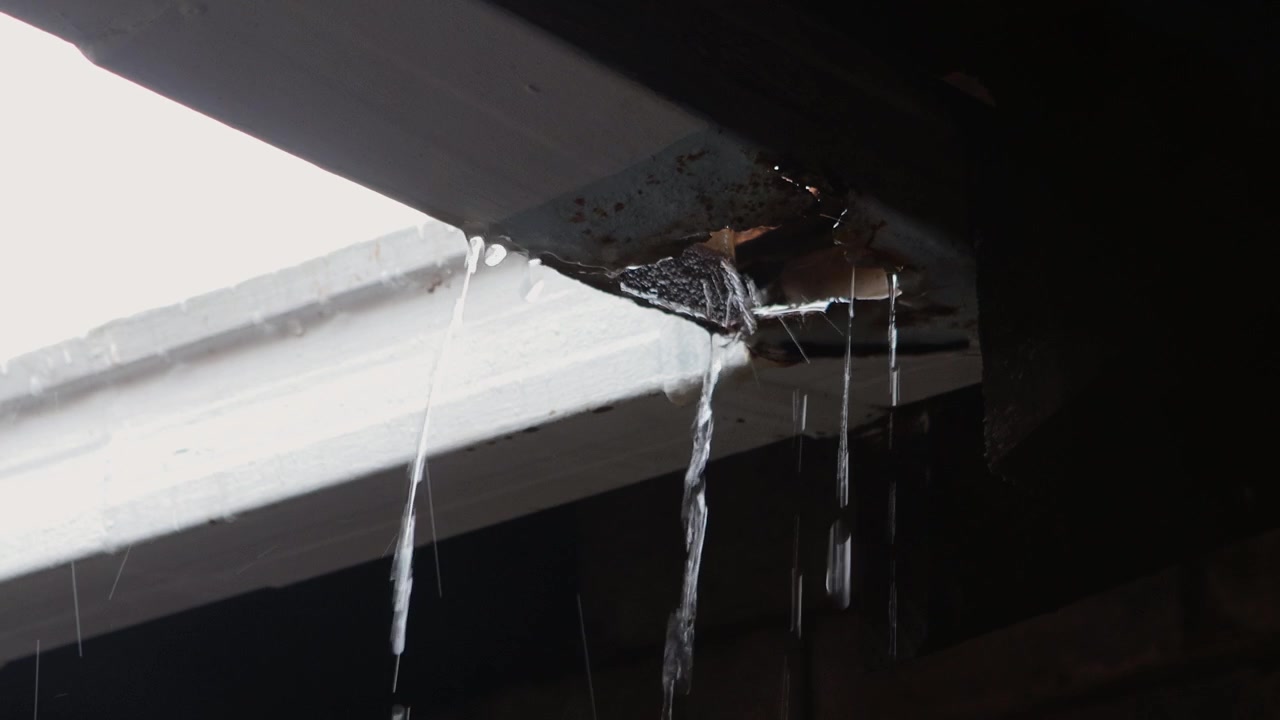 Close-up footage of a damaged gutter leaking heavily during a rainstorm. Water is pouring through a large hole caused by rust and years of neglect, highlighting the effects of poor maintenance.