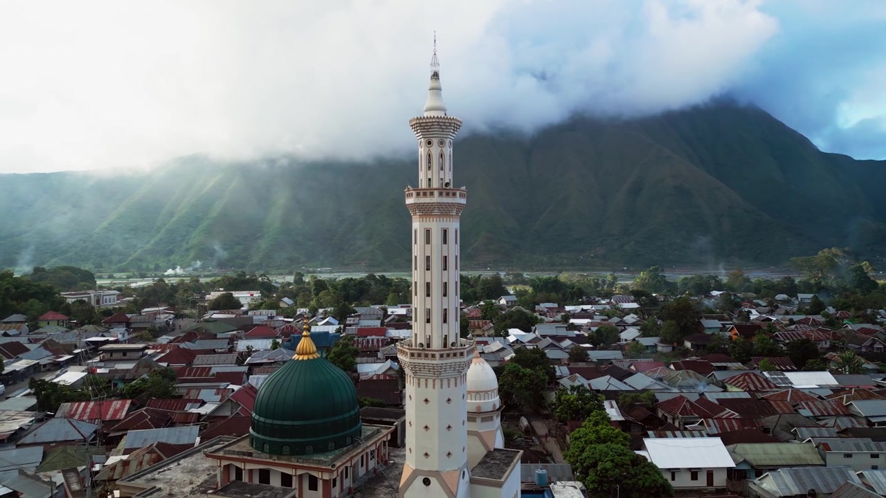Permukiman Islami pedesaan dengan masjid megah dikelilingi rumah-rumah penduduk di bawah lereng gunung berkabut di Sembalun Lombok, rekaman drone udara.