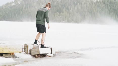 Man-Walking-On-Broken-Wooden-Jetty-From-The-Frozen-Lake-Of-Trondheim,-Norway