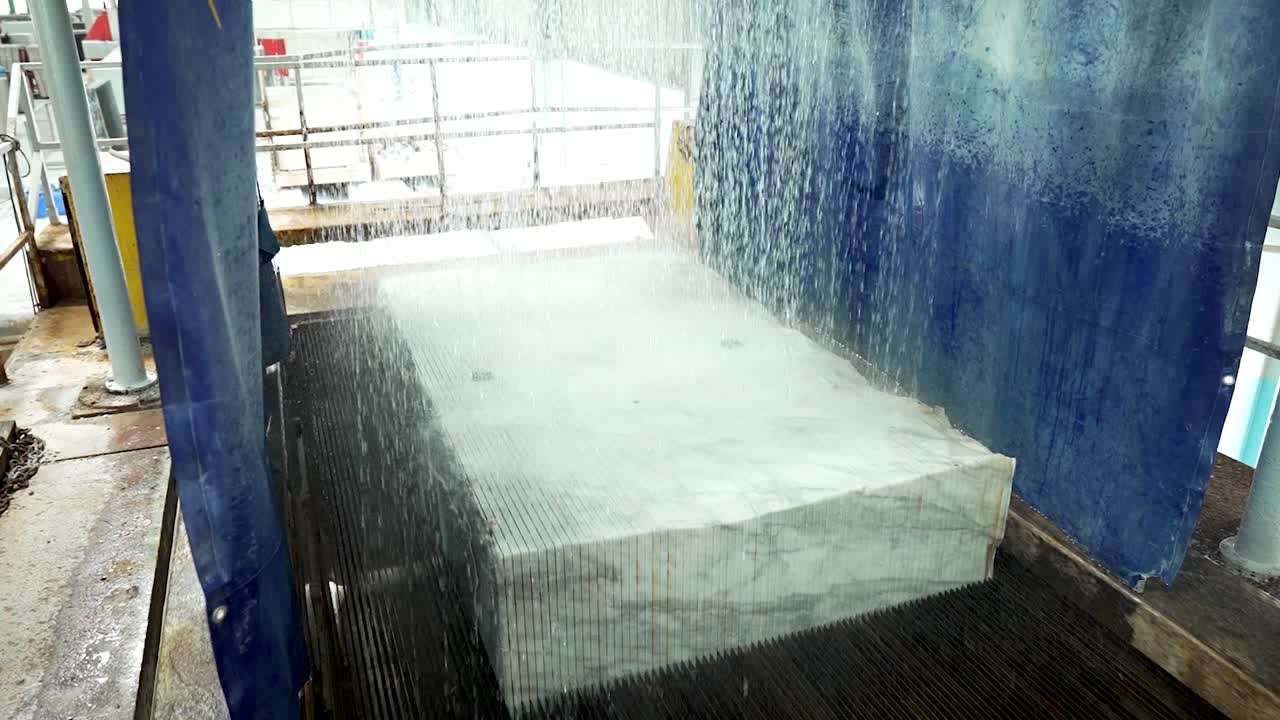 Wide shot of Marble block cutting with water jets in stone processing factory. Industrial marble slab slicing process. Wet stone saw machine, factory production, heavy machinery, marble cutting video