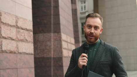 smiling caucasian male journalist speaking on the microphone in the street in autumn