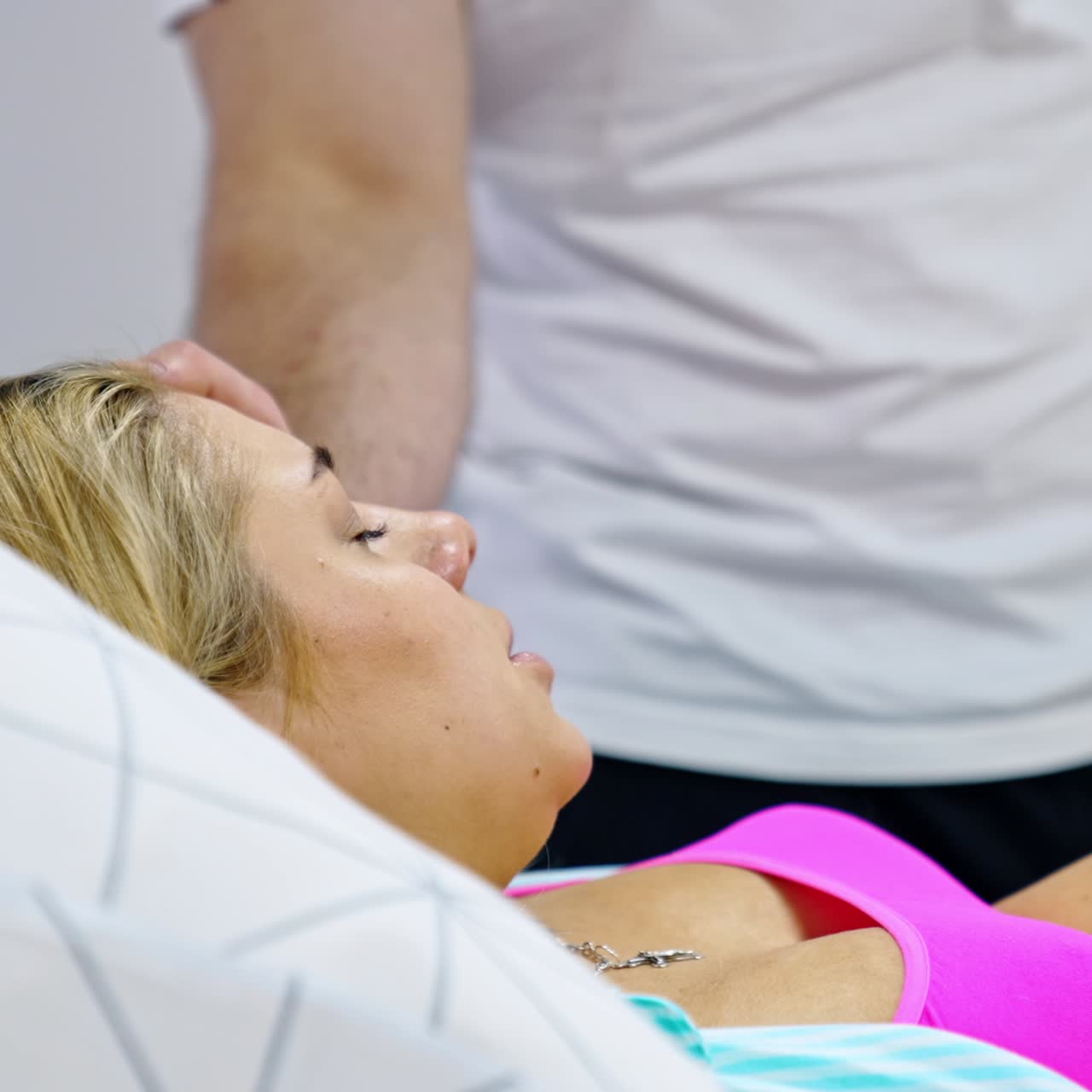 Caucasian woman lies in bed with medical equipment attached to her big belly. Lady feeling bad from contractions. Man at backdrop comforts his wife