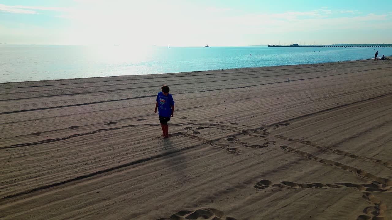 Boy writes name in sand with Bare Feet on warm sunny morning beach. Drone shot