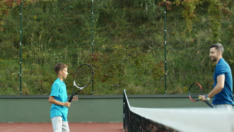 Side-View-Of-Dad-And-Teen-Son-Laughing-And-Cheering-Before-Or-After-Tennis-Game-Outdoors-At-Sport-Court