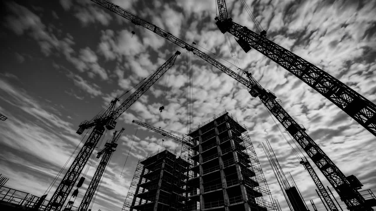 Dramatic low-angle video shot of construction cranes and buildings against a cloudy sky