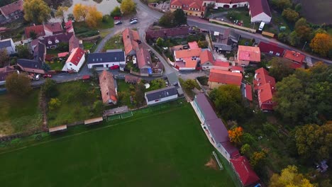 Drone-view-captures-view-of-town-by-moving-backwards-with-houses,-lush,-trees,-roads,-football-ground