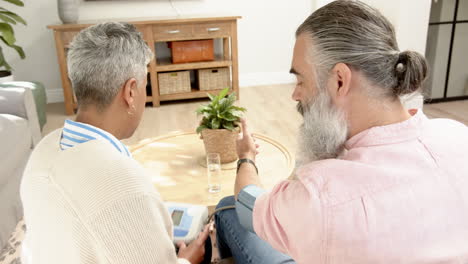 senior couple using blood pressure monitor, discussing health in living room