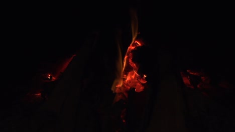 embers of coal glowing red hot with small flames burning in wood fire, filmed as close up in slow motion