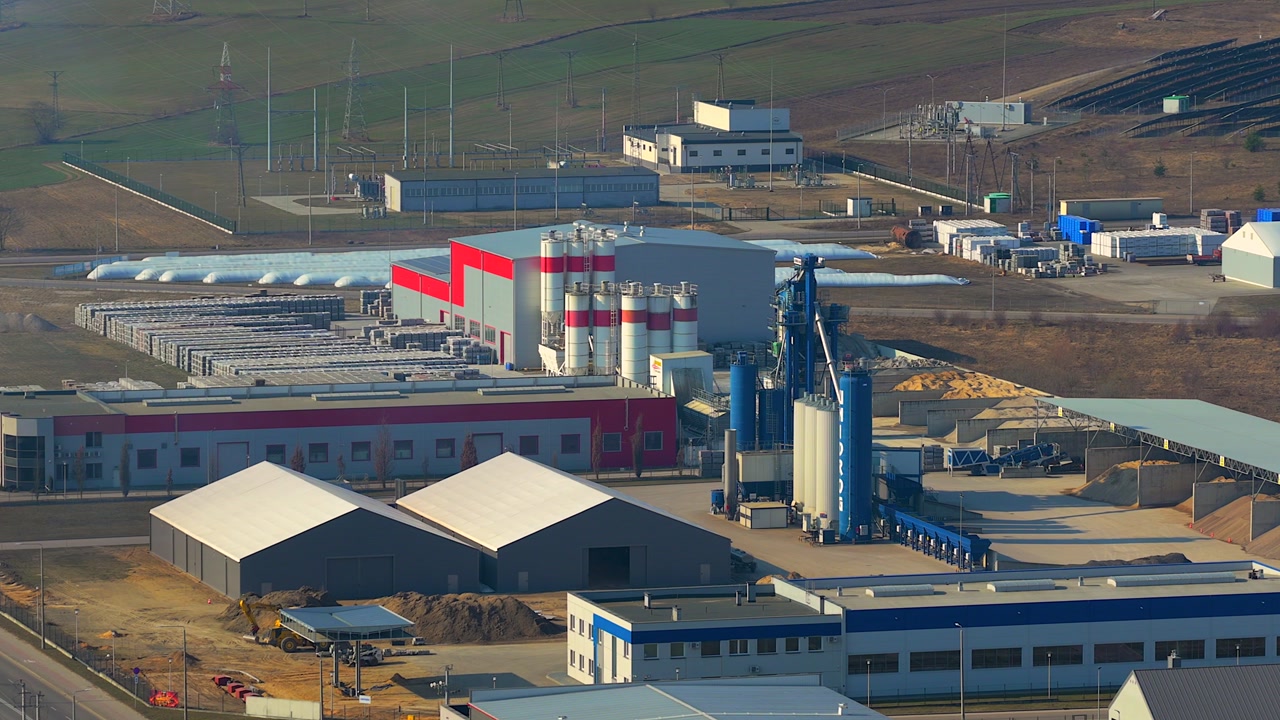 Establishing aerial shot of a large sand and cement manufacturing plant. The industrial complex includes silos, warehouses, and conveyors